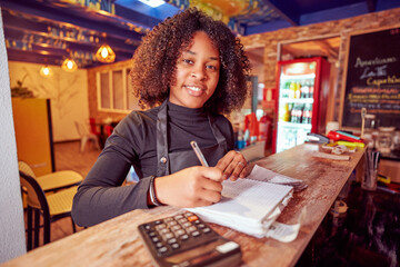 African American smiling waitress writing customer order in cozy coffee shop	