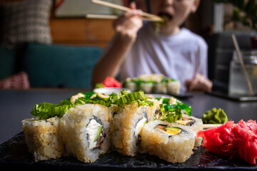 Closeup hand holding bamboo chopsticks with nigiri shrimp while soaking it in soy sauce. Detail of sushi set on wooden tray at restaurant while hand dip nigiri in soy sauce. Japanese cuisine concept.