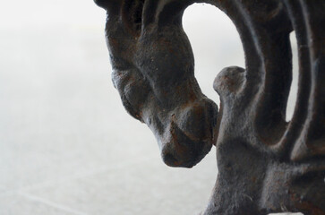 Cavalo metálico de ferro enferrujado e desgastado visto de perto. Ornamento que enfeita das pernas de bancos de praça 