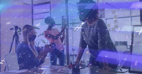 Collaborating three women wearing masks in office checking DSLR camera and reviewing sticky notes