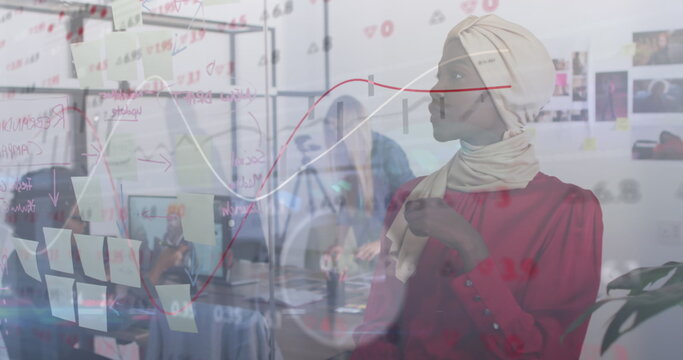 Working woman wearing beige headscarf red blouse adding sticky notes on board in office, copy space - Powered by Adobe
