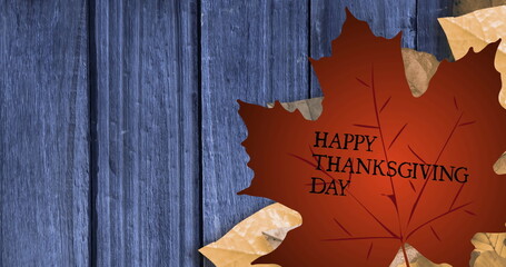Fototapeta premium Featuring large brownish-red maple leaf bearing HAPPY THANKSGIVING DAY on blue planks, copy space