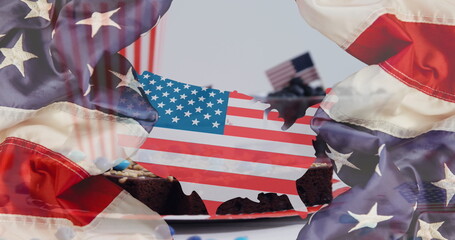 Displaying US flag cutout hovering over brownies with toothpick flags on table, with flag backdrop