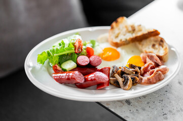Full English breakfast on a white plate with fried eggs, bacon, sausages, mushrooms, toast, and fresh salad. Colorful and appetizing meal shot from above.