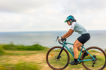 Obraz premium Latin cyclist woman riding gravel bike by the sea at sunrise