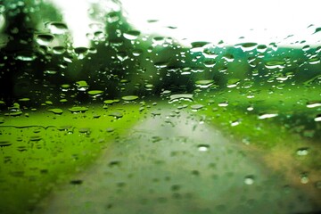 Abstraktes Motiv mit Regentropfenmuster vor grüner Landschaft mit asphaltiertem  zwischen grüner Wiese vor Bäumen und Himmel mit Licht bei Regen und Sturm am Nachmittag im Frühling
