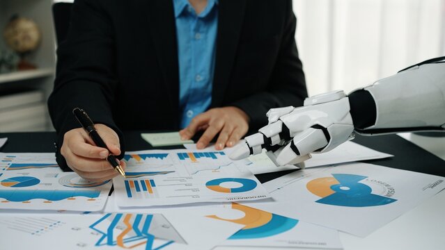 A human and a robot collaborate to analyze financial reports, highlighting the fusion of technology and business efforts in a modern workspace, symbolizing innovation.Noogenesis