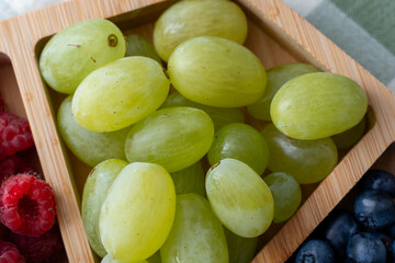 Close-up of fresh green grapes in wooden tray with raspberries and blueberries. Concept of healthy...