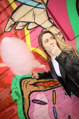 Young woman enjoys cotton candy in front of vibrant street art during a sunny day at a local fair
