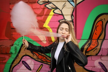 Young woman enjoying cotton candy in front of a colorful urban mural during a sunny day