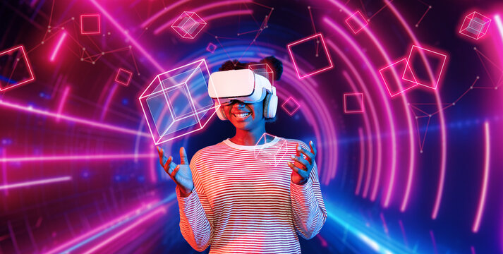 Girl looking around at geometric shape floating in metaverse. Happy teenager or gamer using VR headset and augmented reality technology accessing virtual world. Technology innovation. Ingenuity.