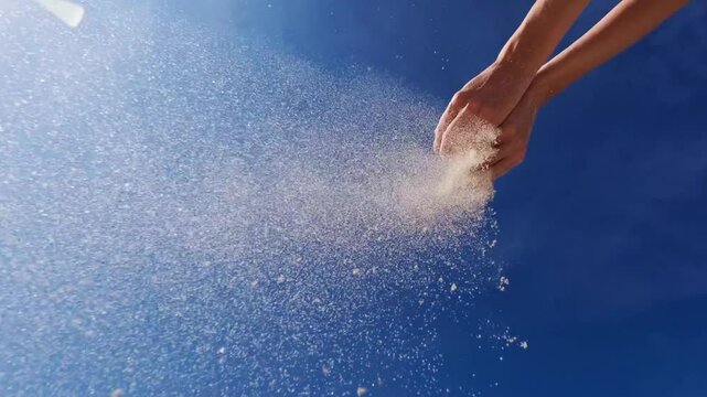 Woman pouring sand from hand on beach, blue sky.
