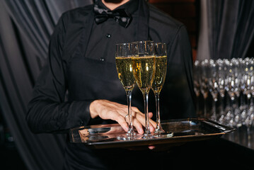 Waiter serving champagne flutes at formal event. A waiter in black attire carries a tray with glasses of champagne during a formal celebration or upscale gathering.