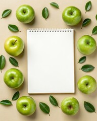 Captivating flat lay of fresh green apples and lush leaves surrounding a blank notepad on beige background for creative inspiration.
