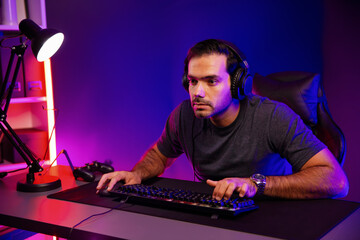 Smart gaming streamer concentrating gaming players trying to pass the level at mission completed, using headset and mic for communicate others on streaming live at neon lighting studio room. Surmise.