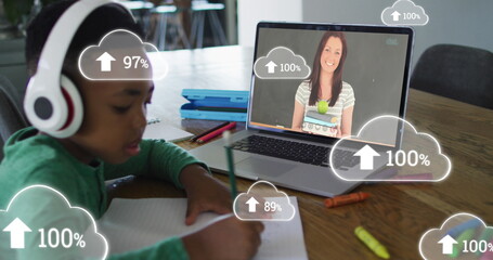 Writing child wearing white headphones working at table with laptop cloud icons, copy space