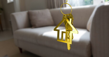 Dangling golden house-shaped keyring holding metal keys in living room, with beige sofa, copy space