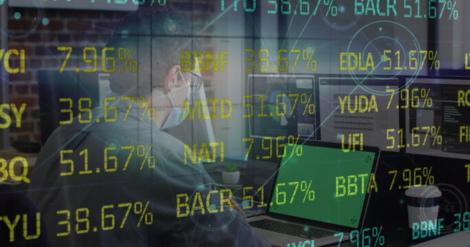 Analyst wearing hoodie mask and glasses analyzing data in home office with dual monitors and laptop