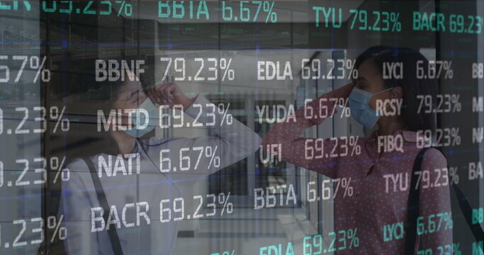Elbow bumping two masked businesswomen exchanging greeting at transit hub, ticker display