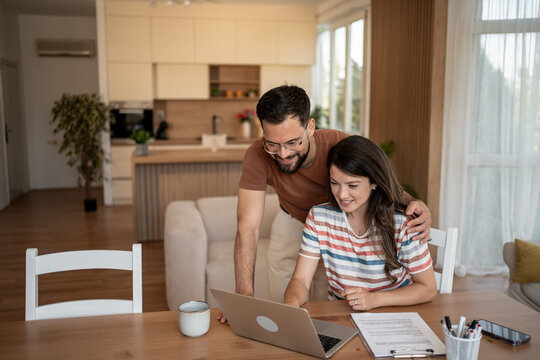 Happy couple doing finances and calculating bills at home using laptop