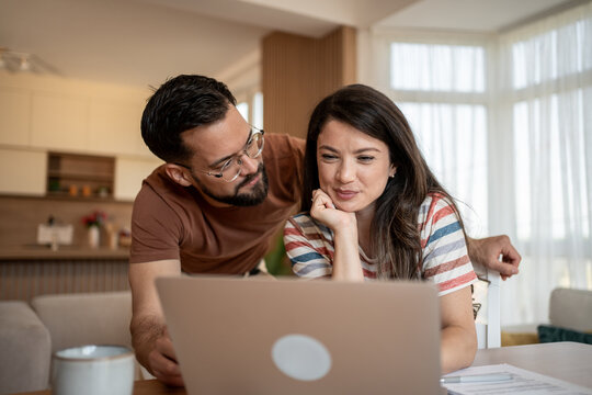 Couple managing finances at home using laptop: concentrated young couple reviewing domestic budget on laptop in living room
