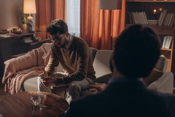 Upset man sits on couch sharing experiences with psychologist, consultation