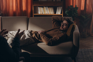 Male patient rests gesticulating on couch sharing thoughts with psychotherapist in therapy room