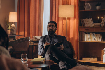 Man psychologist sits in chair with notebook observing interaction of married couple