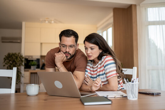 Focused couple reading important information on laptop at home