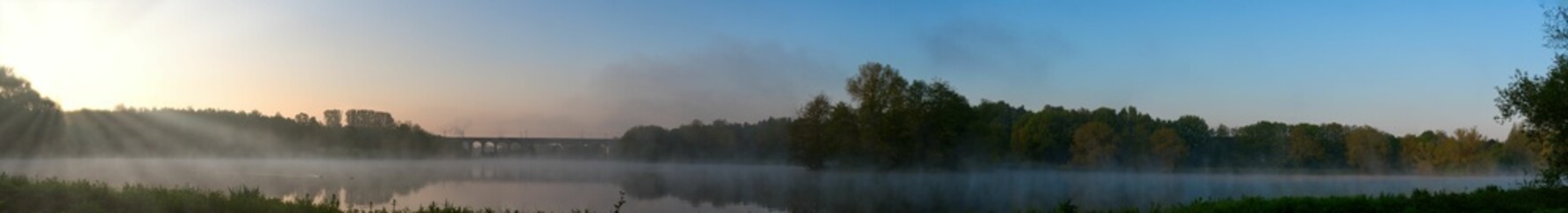 panoramic shot of a lake in the morning at sunrise with light fog