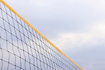 Beach volleyball net close-up. Fragment of a volleyball net on the beach against a cloudy sky. Sport, beach volleyball. Active recreation concept. Sports ground. Active summer games. Sports equipment