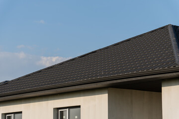 A modern building features a sleek dark metal roof under a clear blue sky during the afternoon, highlighting its contemporary design