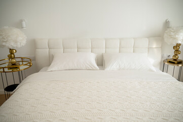 Bright bedroom with white pillows with a blanket and a plaid on the bed, a bedside table with a lamp