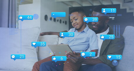 Smiling father and son watching tablet in modern living room, with floating social media icons