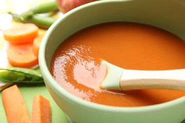 Baby food. Tasty puree in bowl and ingredients on green background, closeup
