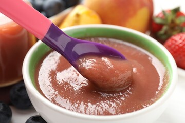 Baby food. Eating tasty puree with spoon at white table, closeup