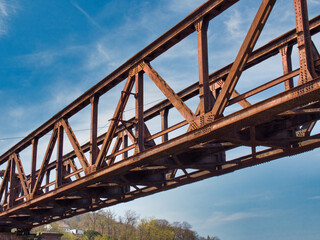 Rusty metal truss bridge under a sunny blue sky full of clouds