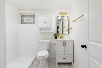 A bathroom with a pattern tile floor, white cabinet with gold faucet and hardware, and a shower white subway tile shower.
