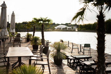 Outdoor lakeside patio seating surrounded by palm plants during sunset