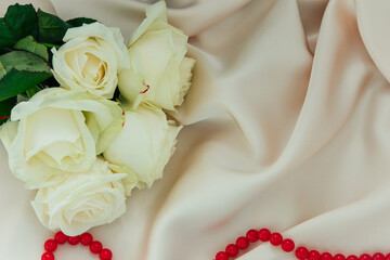 Elegant white roses and red beads displayed on soft satin fabric at a romantic setting