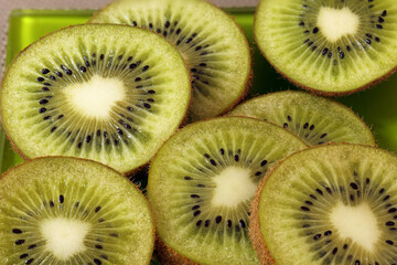 Sliced kiwi fruits arranged on a green plate. The vibrant green flesh is dotted with small black...