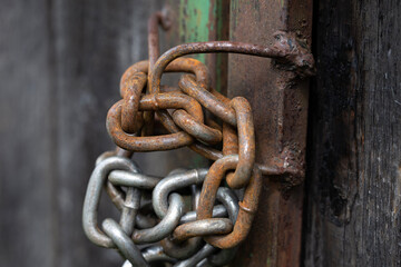 A close-up of a rusty padlock secured with a chain on a wooden door. The door has a weathered...
