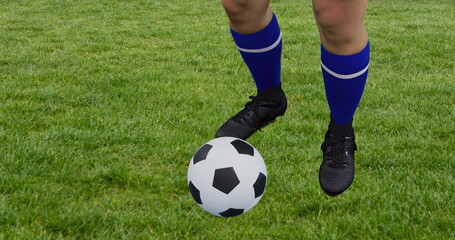 Dribbling soccer ball with player's lower legs in blue striped socks, cleats on green grass field