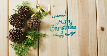 Pinecones with evergreen sprigs resting on wood panel, gold ribbon and teal greeting, copy space