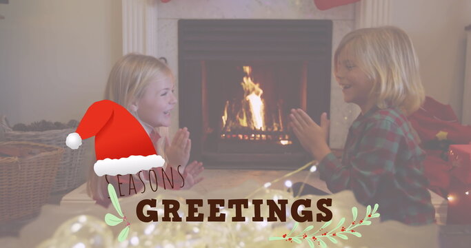 Siblings playing clapping game in living room with lit fireplace, hanging stocking on marble mantel - Powered by Adobe