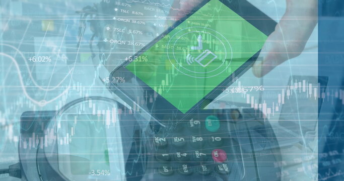 Holding smartphone showing payment icon hovering over card reader at checkout with financial charts