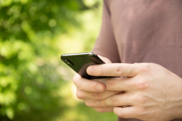 Close up of mans hands holding smartphone in outdoor green setting. Check apps, focused on device, chatting, texting or browsing internet.