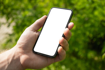 Man hand holding mobile phone with white blank screen against blurred green background. Showcasing mobile apps, design mockups, or digital content presentations. Check apps. Summer heat weather.