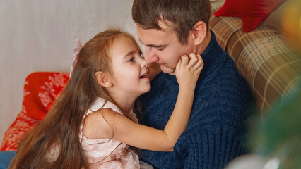 Portrait of a loving daughter kissing her father near the Christmas tree and celebrating Christmas at home.