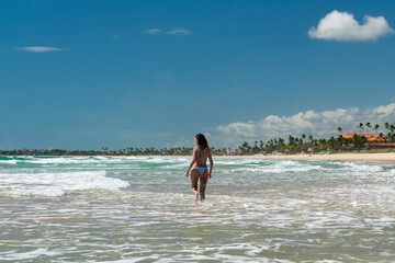 Young woman in white bikini swimming in greenish sea on deserted beach on sunny day